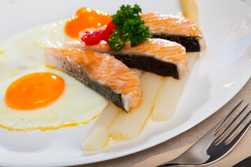 Hearty breakfast of fried eggs with salmon and steamed asparagus garnished with tomatoes and fresh greens..