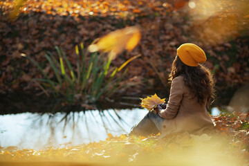 Seen from behind stylish woman in beige coat and hat sitting