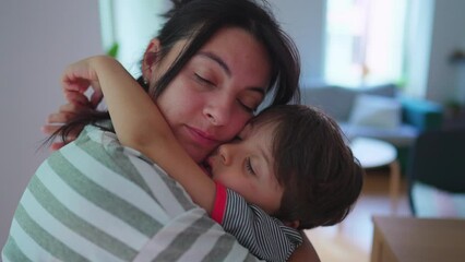 Mother holding little son in tender loving embrace at home. Child with arm around affectionate mom, cheek to cheek in authentic love