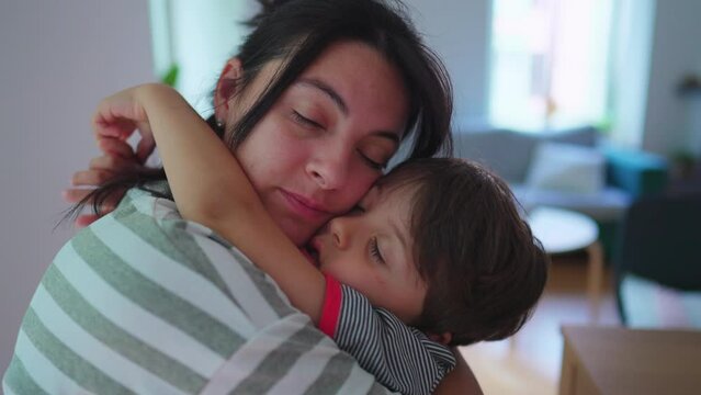 Mother holding little son in tender loving embrace at home. Child with arm around affectionate mom, cheek to cheek in authentic love
