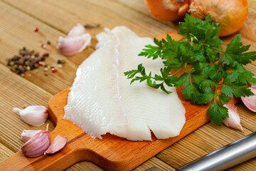 Fresh halibut fillet on wooden surface with seasonings prepared for cooking