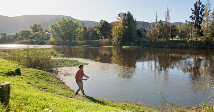 Nature, man and throwing rocks into a lake for fun, summer and activity on a vacation. Youth, teenager and a person with a stone in a river while on holiday or camping in the countryside in spring