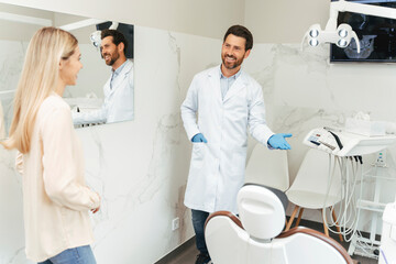 Obraz premium Portrait of dental man and beautiful female patient in dental office, standing near dental chair