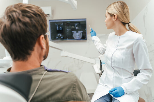 Portrait of female dentist doctor showing x-ray picture to patient sitting in dental chair in clinic