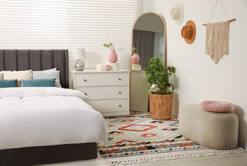 Comfortable bed with cushions, houseplant and different decor elements in room. Stylish interior