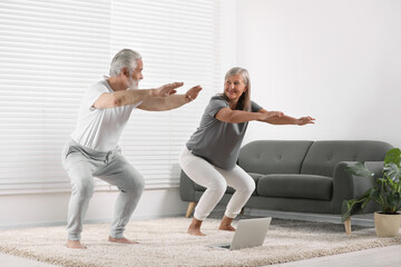 Senior couple practicing yoga with laptop on carpet at home