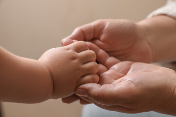 Woman holding hands with her granddaughter on beige background, closeup