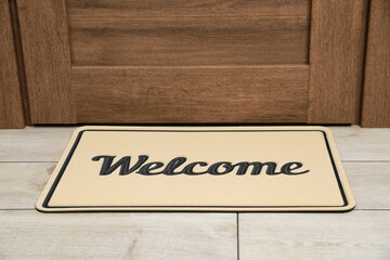 Obraz premium Beautiful beige doormat with word Welcome on floor near entrance