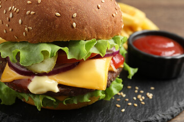 Delicious burger with beef patty and tomato sauce on dark board, closeup