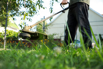 Man cutting green grass with string trimmer outdoors, closeup