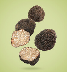 Cut and whole truffles falling on olive color background