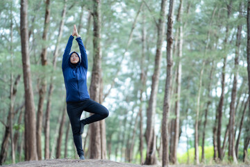 Athletic Asian Muslim Sports Woman Wearing Hijab and Sportswear relaxes in yoga pose in green nature park, Healthy and lifestyle concept, Muslim yoga concept.