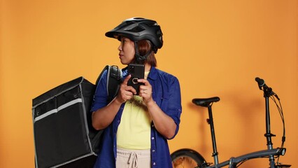 Confused asian woman looking around for directions, unsure of client location whereabouts. Professional courier wearing thermic backpack riding bike to deliver food, isolated over studio background - Powered by Adobe