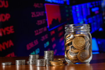 Coins in a glass jar, a pile of coins on a financial market chart in the background.