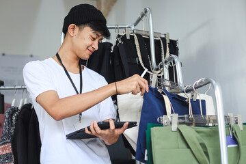 Young Asian man working as shop assistance at retail shop, holding digital tablet for checking stocks.