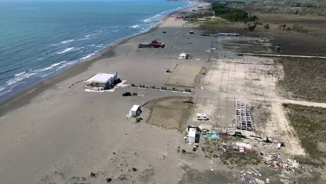 Top view of deserted Great beach Ulcin, grey volcanic sand, waves on sea, infrastructure buildings in off season. Closing of resort, filming from a drone slow motion along the coastline of the coast