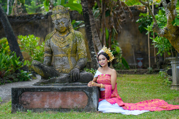 Beautiful Woman siting in front of a Buddha statue in a red costume and a crown in hair