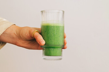 Close-up of female hand holding a glass with freshly blended green smoothie isolated over white...
