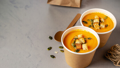 Thick vegan pumpkin cream soup with seeds and croutons in disposable cups of craft paper. Soup to...