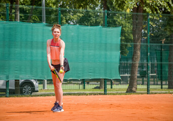A young woman playing tennis is preparing to serve the ball. Open ground.