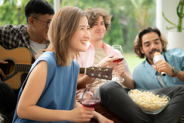 Multiethnic group of friends having fun playing guitar and singing together at home