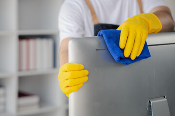 Person cleaning room, cleaning worker is using cloth to wipe computer screen in company office...
