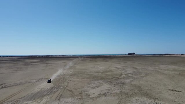Aerial drone backward moving shot of a tourist vehicle driving through sandy Sapat beach, buji koh, Balochistan on a sunny day.