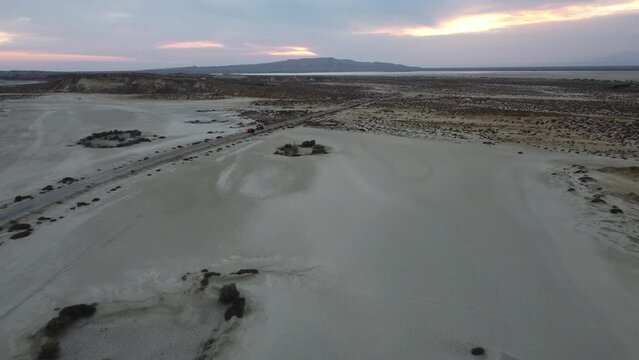 Aerial drone forward moving shot over dry arid landscape road with vehicle driving towards Mud Volcano in background at Hingol National Park in Balochistan.