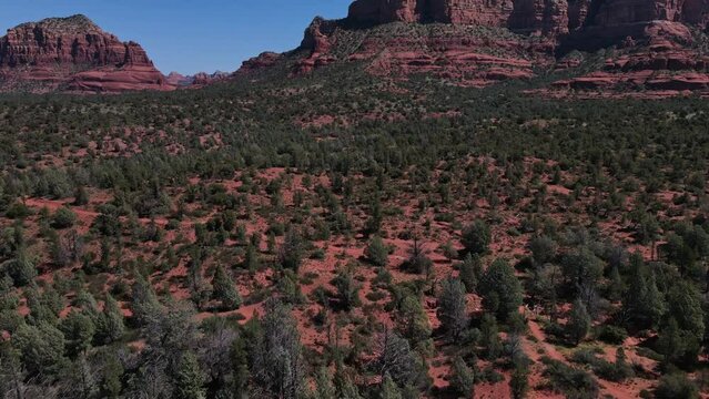 Aerial drone flying over desert brush in Sedona, Arizona and panning up to reveal red sandstone formations with Chicken Point Overlook in the distance.