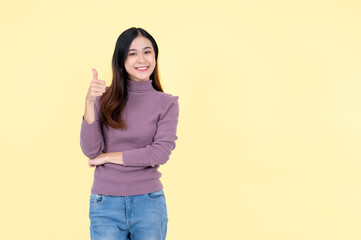 A beautiful Asian woman shows her thumb up and stands against an isolated yellow background