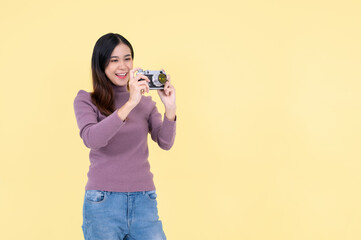 A happy Asian woman is taking a photo with her vintage film camera, isolated yellow background