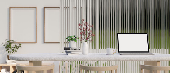 A laptop mockup on a white tabletop with a coffee cup, books, and flower vase in a modern room.