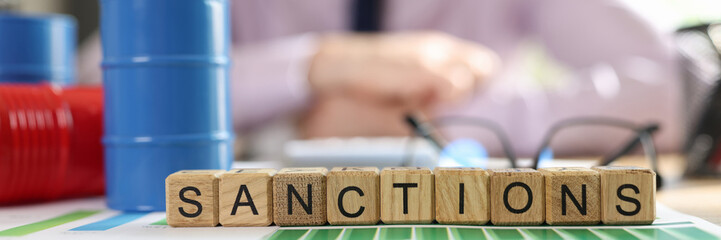 Word sanctions collected from cubes on financial reports, barrels of oil and manager in background.