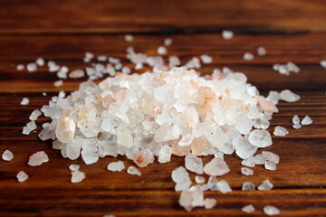 A pile of large pink salt lies on a wooden background.	