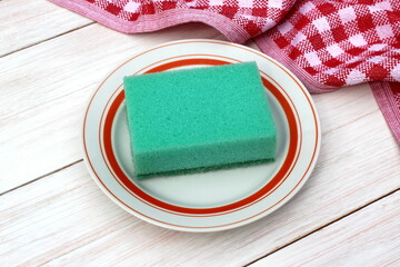 
There is a plate with a sponge for washing dishes on a wooden table.
