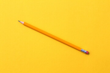 A simple pencil lies on a yellow background.