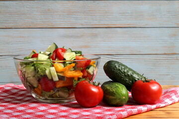 Tomatoes and cucumbers lie on the table against the background of a bowl of salad.	