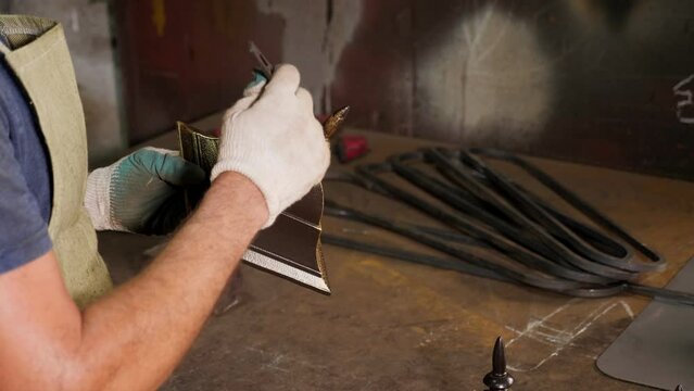 A close-up of a blacksmith man paints scratches and roughness on the bell with gold powder, creating an aging effect. Pattern on iron. Carving ornament.