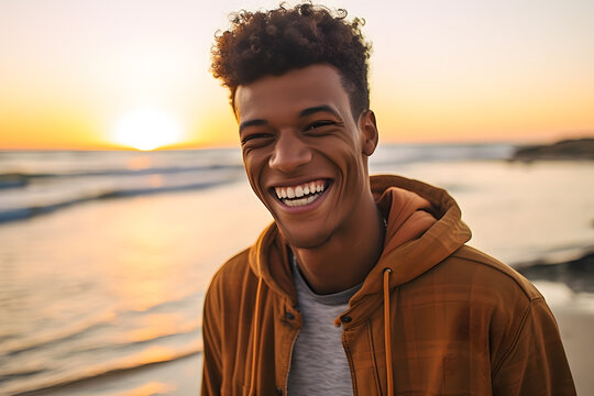 An African young man in buff color hoody smiling happily on the beach at sunset 