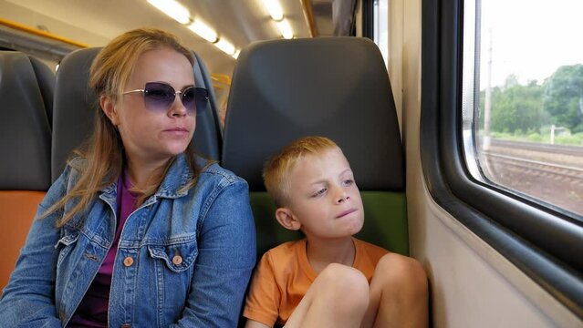 Portrait of a mother and son on a train, they are sitting in a chair and looking out the window, the family is traveling by train. Mother and child in the train.