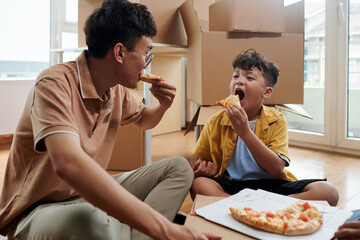 Hungry father and son eating pizza in their new apartment