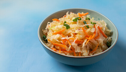 Homemade Sauerkraut with carrots and green onions in a bowl on a light blue background, Fermented food