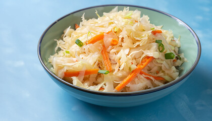 Homemade Sauerkraut with carrots and green onions in a bowl on a light blue background, Fermented food