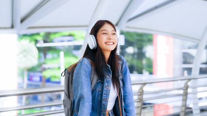 Portrait of happy young asian woman listening music online with wireless headphones from a smartphone in the city