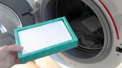 Woman putting a sheet laundry detergent into a washing machine - Powered by Adobe