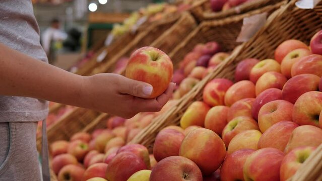 Close-up of a woman choosing red apples in a supermarket. A woman's hand with a red apple in a grocery store. 