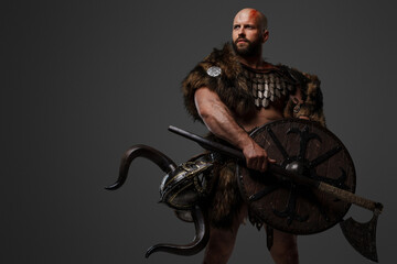 A rugged, bald, bearded Viking dressed in fur and light armor, with a helmet attached to his belt,...