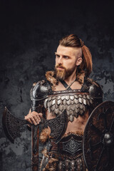 A fearsome bearded Viking dressed in fur and light armor, wielding an axe and shield against a grey textured wall