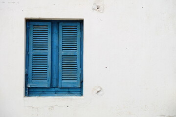 Blue window with wooden shutters on a white stone wall