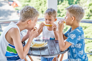 Junior school children and preschooler boy eating fresh melon on hotel terrace. Brothers spend together summer holiday at sea resort - 632450379